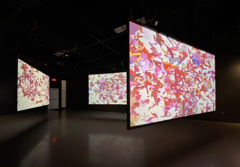 Installation consisting of three large projected screens of abstract pink and red shapes on white.