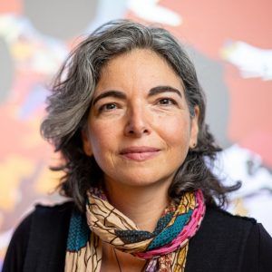 A close up photo of artist Nayda Collazo-Llorens. She wears a vibrant scarf and smiles at the camera.