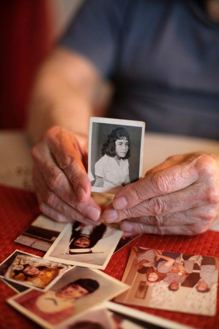 An older person holds up a black and white photo of a young woman out of a pile of other old photographs.