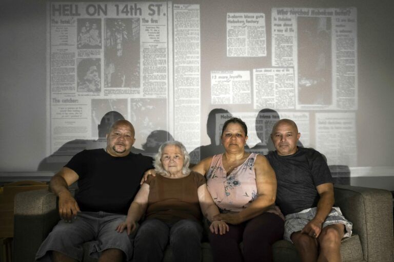 Four people, two women and two men sit on a couch while a newspaper that reads "Hell on 14th St." is projected onto their faces and bodies.