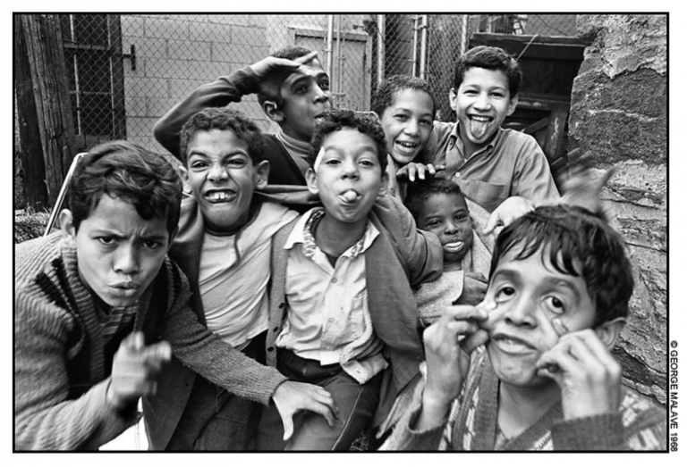 A group of 8 young children sticking their tongues out, pulling on their cheeks, and making faces.