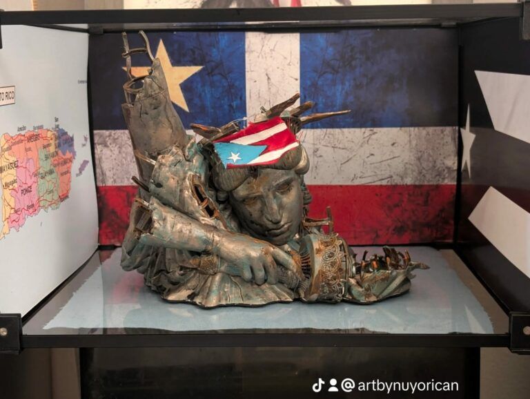 Statue of Liberty old and broken with the Puerto Rican flag over her forehead and the Grito de Lares flag behind her.