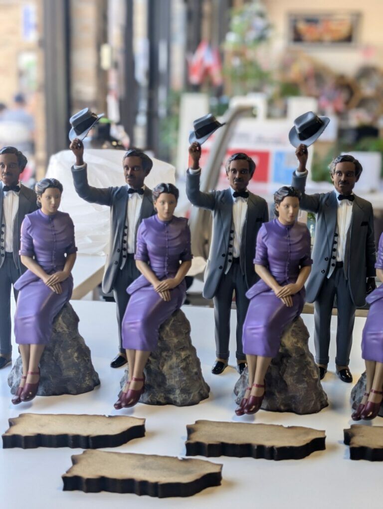 A few statues lined up of Don Pedro Albizu Campos standing holding his hat up and Julia De Burgos sitting down.