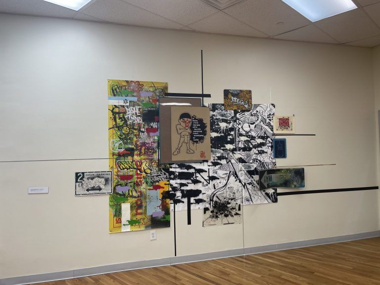 "If Taino, I'd be that guy off to the side muttering I ain't worshiping no turtle." Print of a Taino person wearing Nike sneakers. The print is surrounded by graffiti and signage (one way and parking signs).