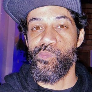 A close up photo of artist FEEGZ. He wears a hat and faces the camera with his lips pursed to the side.