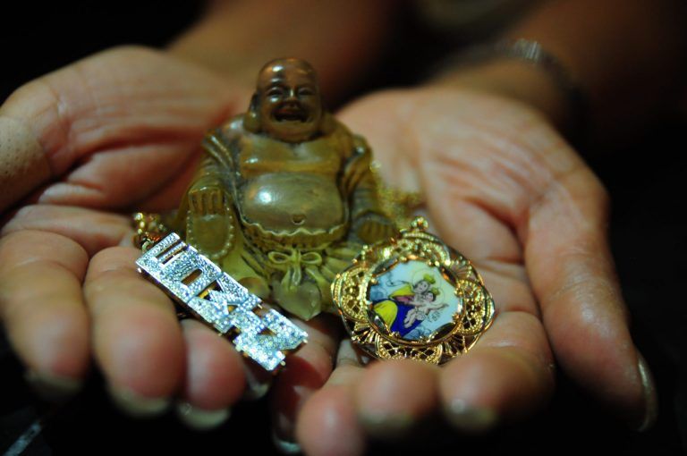 The artist's aunt's hands holding out assorted objects. "The objects include her father's gold & diamond nameplate, a small Buddha statue, and a gold and enamel pendant of the Virgin Mary & Jesus which belonged to her grandmother, her father's mother." - Christina Delgado