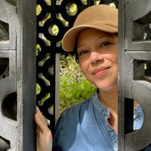 A close up of artist Edra Soto partially behind quiebrasoles. She wears a hat and smiles at the camera.