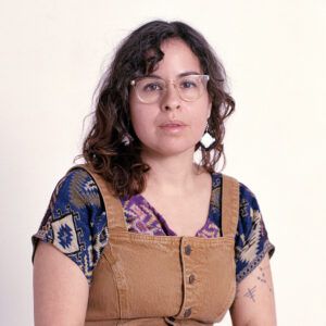 A headshot of artist Estefania Velez Rodriguez. She wears glasses and looks at the camera with a neutral expression.