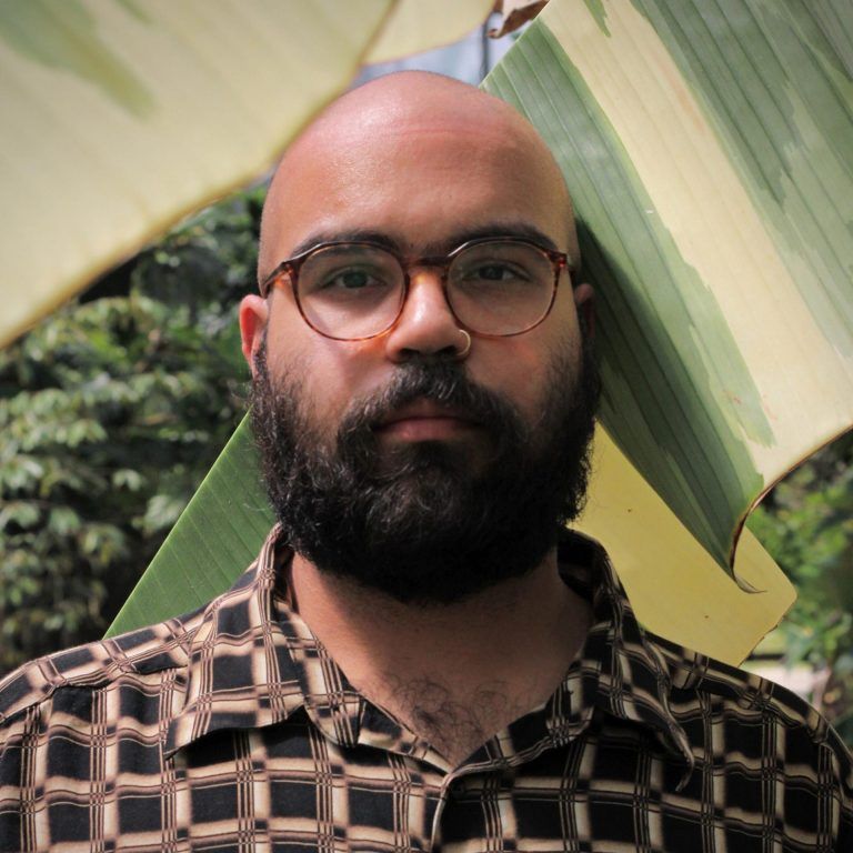 A close up photo of artist Jacoub Reyes. He wears glasses and looks into the camera with a neutral expression.