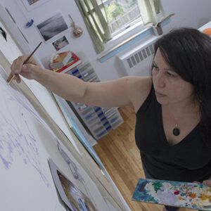 A photo of artist Josie Gonzalez at work. She is looking away from the camera and focused on her painting.