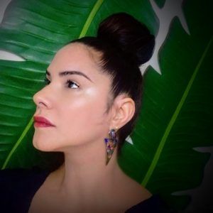 A close up photo of artist Leenda Bonilla in front of elephant leaves. She faces away from the camera with a neutral expression.
