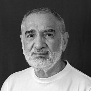 A grayscale close up photo of artist Lope Max Díaz. He looks into the camera and smiles slightly.