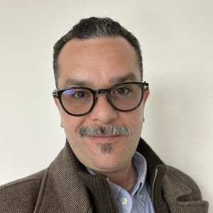 A close up photo of artist Ralph Vázquez-Concepción. They wear glasses and smile at the camera.