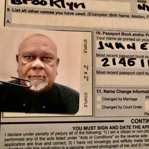 A photo of artist Juan Sanchez attached to his passport application. He looks directly into the camera with a neutral expression.