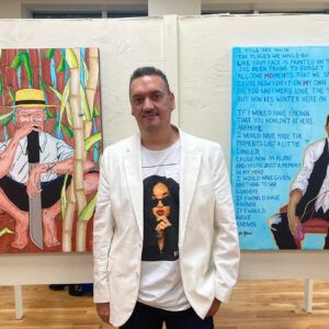 Artist Nelson Host Santiago stands in a gallery displaying his artwork. He smiles at the camera.