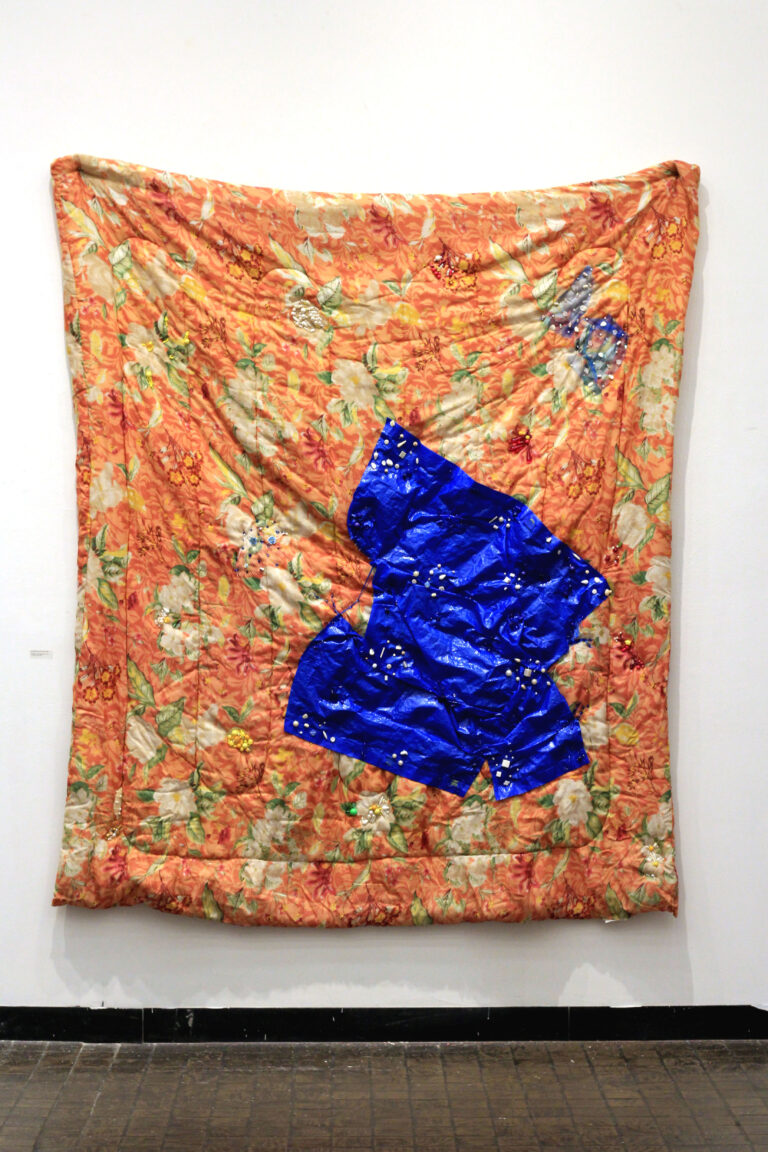 Tarp and produce nets embroidered and beaded onto an orange floral quilted comforter.
