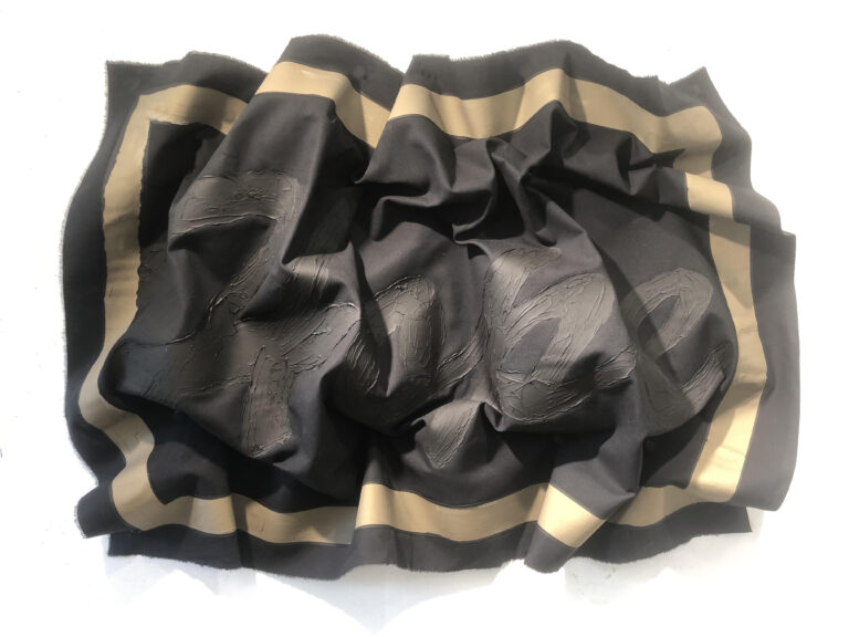 The word "Hope" in grey paint with a tan colored rectangular border around the word against a black canvas. The canvas is crumpled but the word is still recognizable.