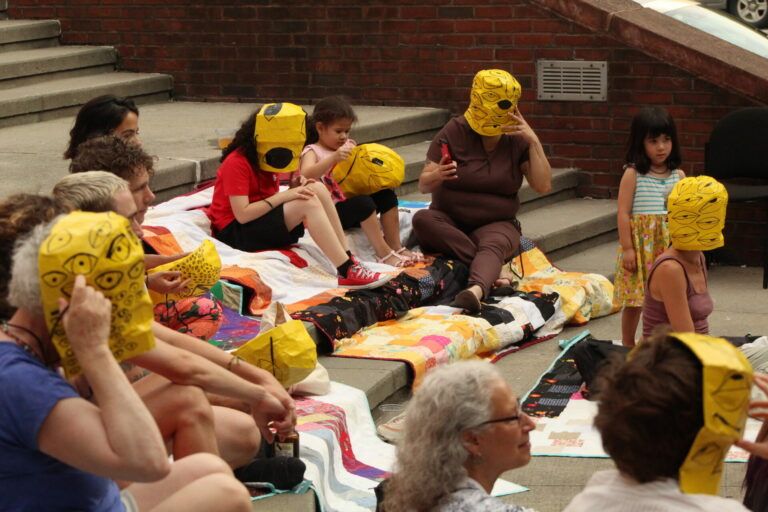 This photo is documentation of audiences wearing the weeping masks as part of a public performance of "I came here to weep," July 2023, at the outdoor amphitheater at Abrons Arts Center.