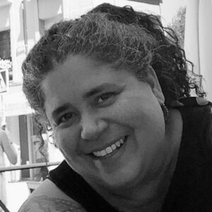 A close up black-and-white photo of artist Brenda Cruz Díaz. She smiles at the camera.