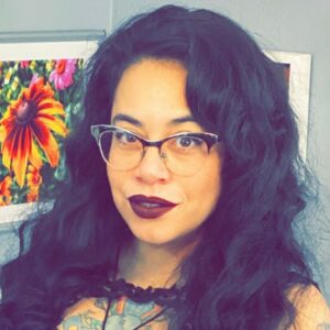 A close up photo of artist Denise Zubizarreta. She wears glasses and smiles at the camera.