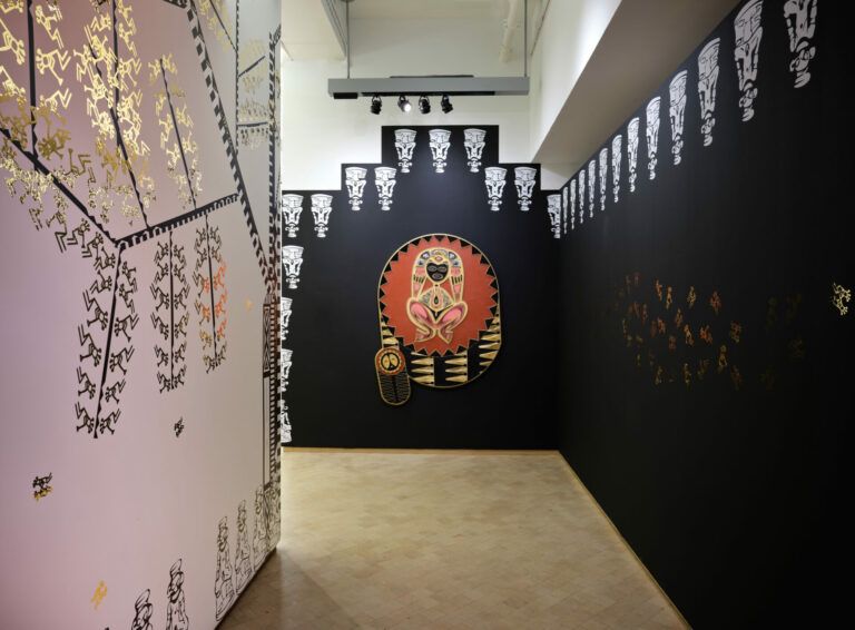 Long hallway with one white wall and one black wall adorned with gold and white Taino symbols. At the end of the hall is the artwork "Atabey."