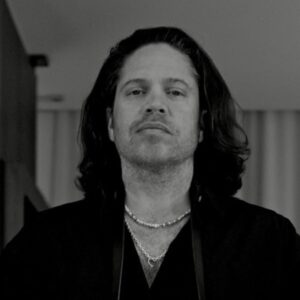 A grayscale close up of artist JuanCarlos Gonzalez. JuanCarlos looks at the camera with a neutral expression.