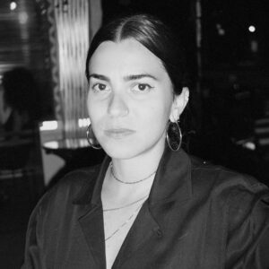 A close up grayscale photo of artist Natalia Almonte. She looks at the camera with a neutral expression.