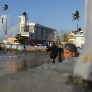 Artist Darice Polo at work. She holds a camera and all but her head is obscured by a wall.