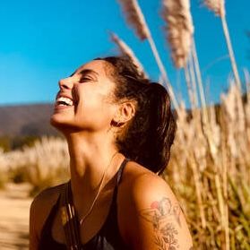 Arist Brianna Elyse Torres stands in a grassy field with her head thrown back in laughter.