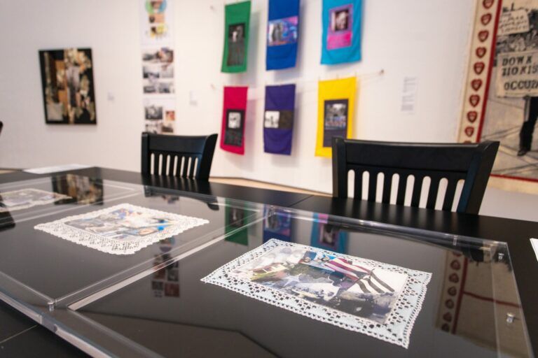 Gallery view of the Diasporic Collage exhibit. In the foreground there is a table with Glorimar Garcia's lacework collages pressed in glass for protection. The background is filled with other colorful collages.