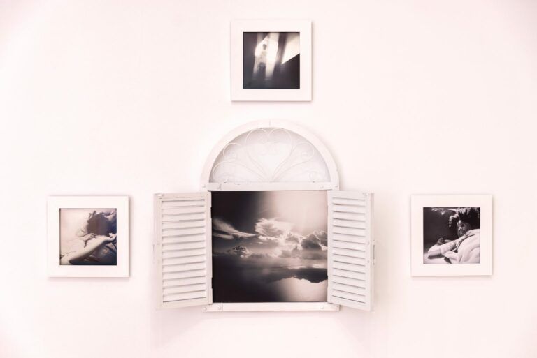 Four black-and-white photographs on a light pink background. The centerpiece is a light pink window with shutters open that contains one of four photos. The photos show a child and the sky.