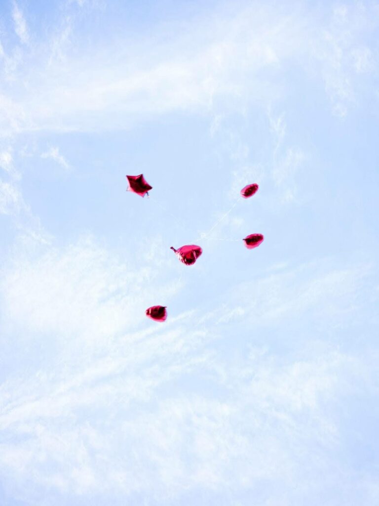 Five red heart and star-shaped balloons float up into a blue sky.