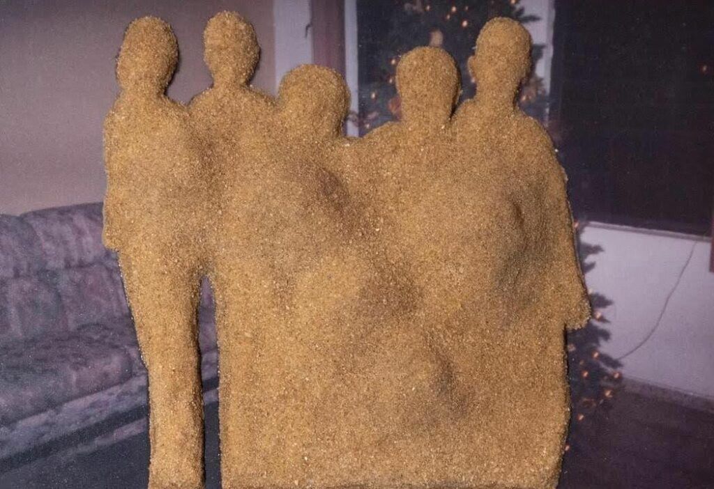 Sand on an image in the shape of five people standing. The image behind the sand contains a Christmas Tree.