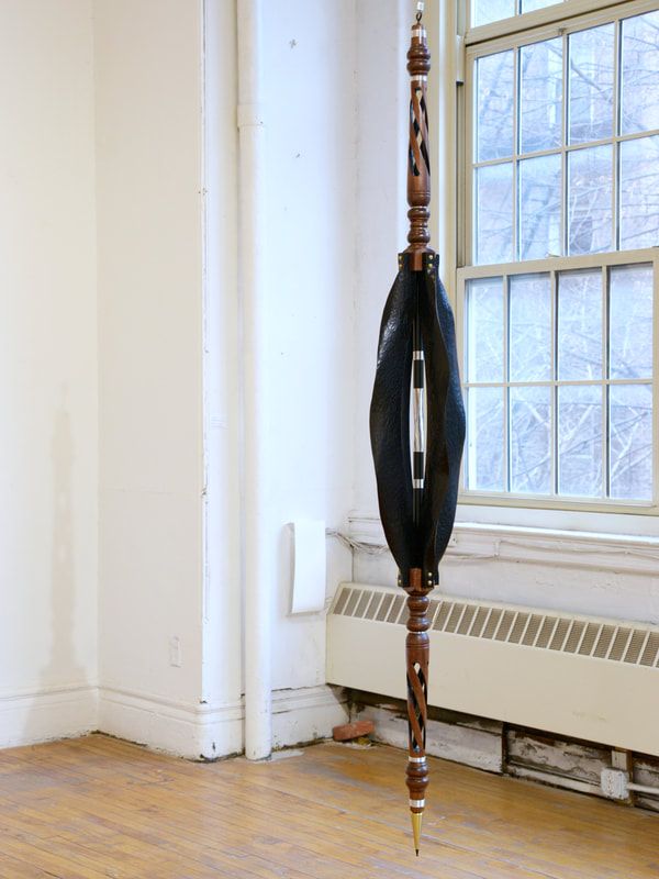 Carved wood, plub bob, and welding wire hung to mimic a pendulum.