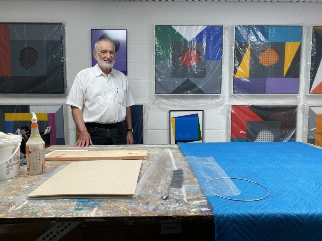 Lope Max Díaz in his studio with plastic wrapped paintings behind him.