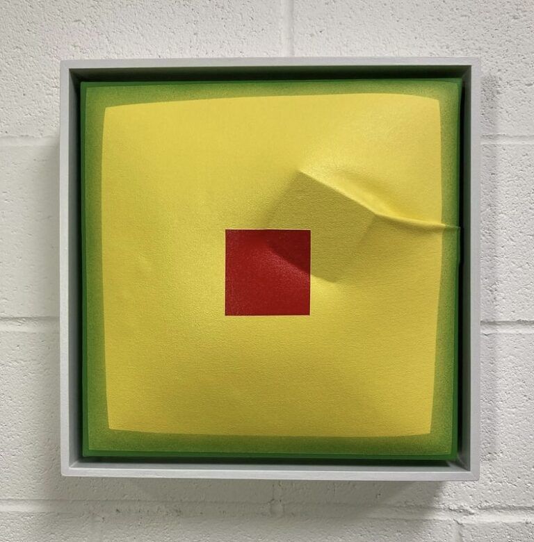Yellow painting with two green borders. The center of the painting has a red square. Underneath the canvas, a cube pushes to the surface.