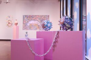 Decorated and painted spiked mace weapons sit on pink display boxes in a gallery.