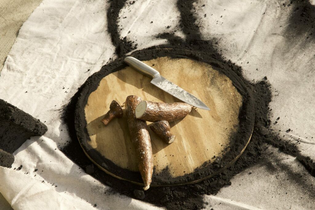 Yucca and a knife on a charcoal-covered cutting board.