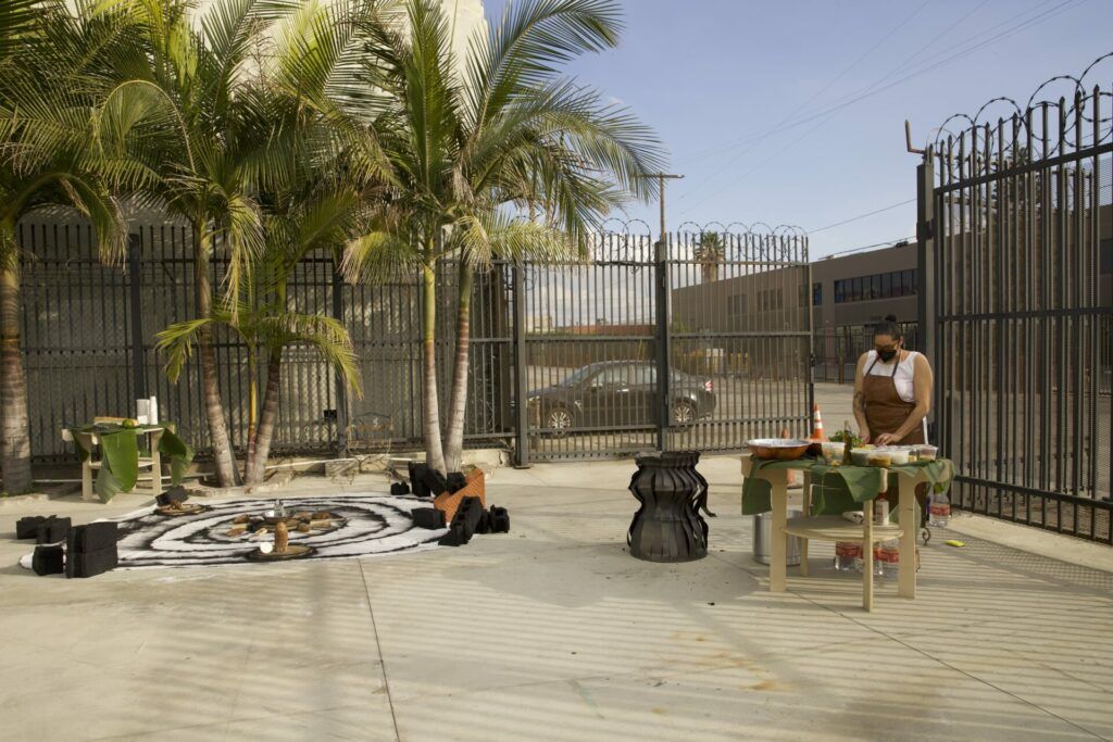 Full view of a cement lot where there is a canvas and materials on one side and Vivas on the other, preparing food.