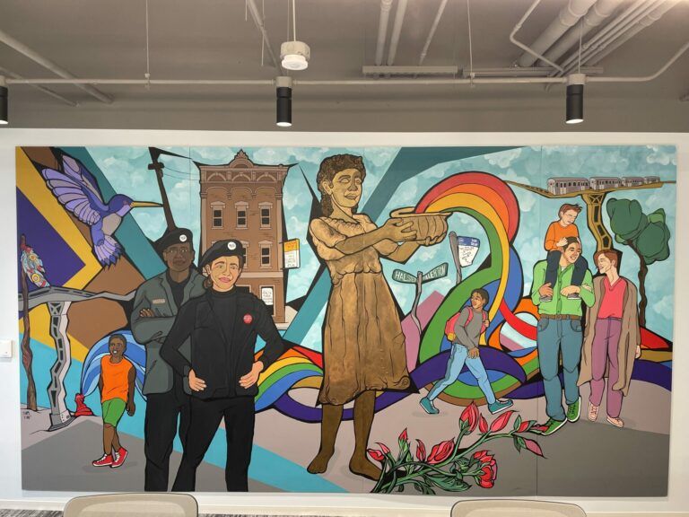 Mural-sized painting of people walking around a statue that holds a rainbow in a bowl overflowing. There's a hummingbird, a MTA train, and a brick building.