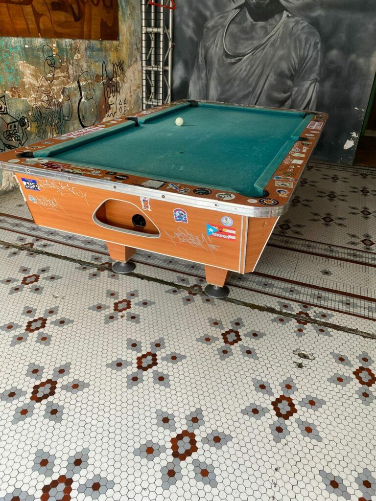 Pool table with Puerto Rican stickers on the aged wood. The tiles under the table is intricate.
